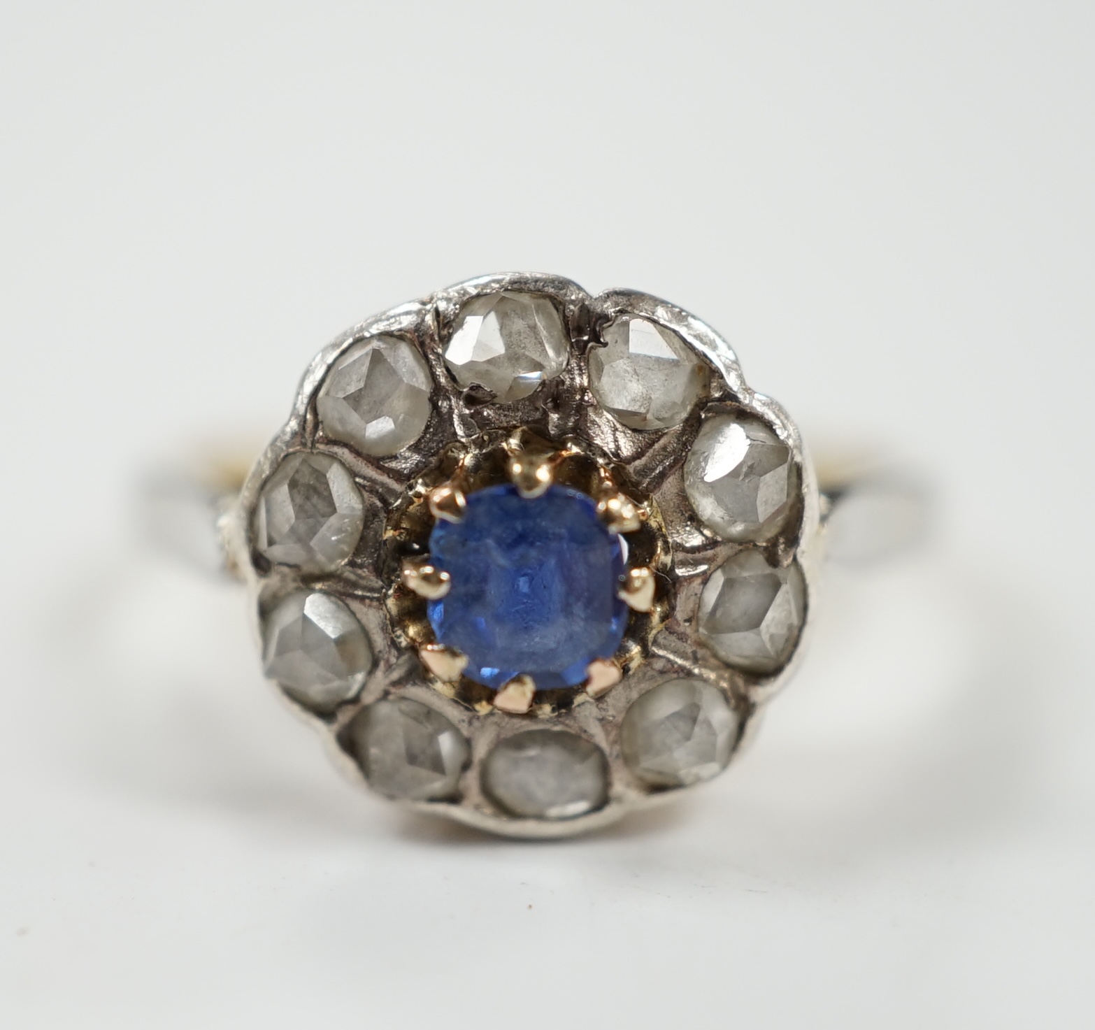 An early 20th century 18ct, single stone sapphire and ten stone rose cut diamond set circular cluster ring, size L, gross weight 3.9 grams.